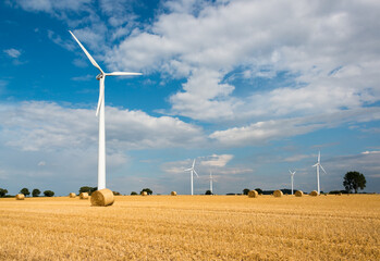 Windkraftanlagen auf einem abgeernteten Getreideacker  und Strohballen im Herbst - 658662769