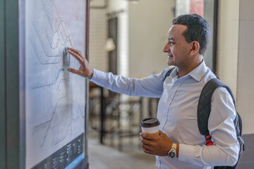 Latino man in shirt looking at train map at train station.