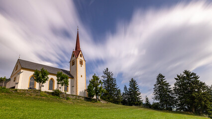 Fototapeta na wymiar eine Pfarrkirche auf einem Berg vor bewölktem Himmel in Tirol