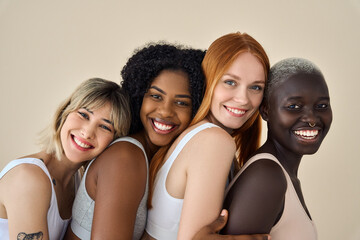 Happy multicultural girls in underwear hugging on beige background, portrait. Smiling positive diverse women, four beauty faces models girls group in underwear bras hugging advertising skin body care.