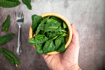 Man holding fresh spinach leaves in a wooden bowl. Background of a gray stone table, top view,...
