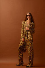 Fashionable confident woman wearing trendy leopard print satin suit blazer, trousers, sunglasses,...