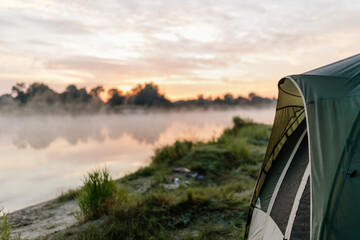 View from the tent of the foggy river in the morning. Camping. Meeting the dawn on the lake.