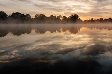 Beautiful landscape with a river and reflection, thick fog at dawn. Lake in the early morning in thick fog