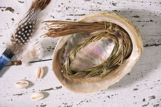 Sweetgrass braid (Hierochloe odorata), also called vanilla grass, in an abalone shell with incense feather on old white wood. High angle view, flat lay.