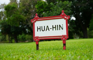 A red metal framed sign with black letters saying Hua Hin, which is a district of Thailand.