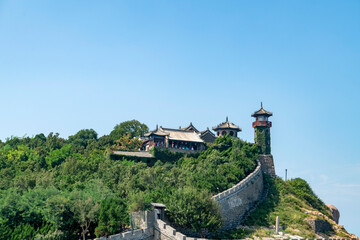 Fototapeta na wymiar The ancient city walls at sea and the watchtower on the mountain, the Penglai Pavilion in Yantai