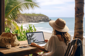 Back view of  woman in hat working on laptop at table on tropical beach, Digital nomad’s lifestyle,  Remote job and teleworking concept, Vacation Leave, Travel visa - obrazy, fototapety, plakaty