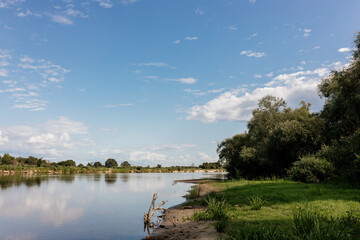 Beautiful summer landscape by the river with blue sky on a sunny summer day. Green grass and trees, on the shore of a lake in the sun. Camping. Summer background.
