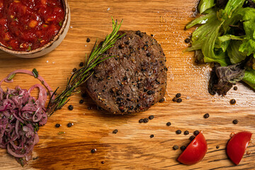 Filet mignon steak served on wooden board with sauce, fresh vegetables, pickled onions and rosemary