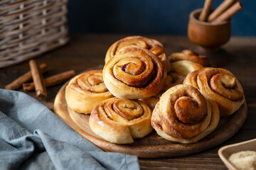 Homemade fresh baked cinnamon rolls on a wooden board with cinnamon sticks, sugar and napkin Wooden...