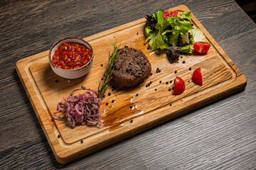 Filet mignon steak served on wooden board with sauce, fresh vegetables, pickled onions and rosemary