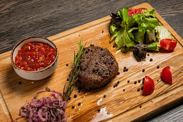 Filet mignon steak served on wooden board with sauce, fresh vegetables, pickled onions and rosemary