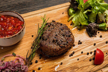 Filet mignon steak served on wooden board with sauce, fresh vegetables, pickled onions and rosemary