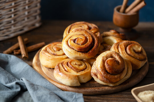 Homemade fresh baked cinnamon rolls on a wooden board with cinnamon sticks, sugar and napkin Wooden and dark background