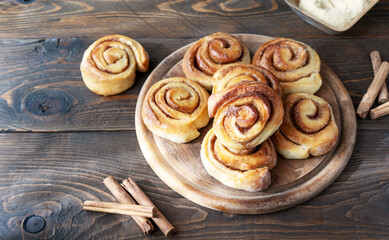Homemade fresh baked cinnamon rolls on a wooden board with cinnamon sticks, sugar over wooden background