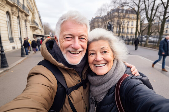 Happy senior couple smiling at camera outdoors,  taking selfie picture with smartphone, life style concept with pensioners having fun together on winter holiday in Paris