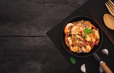 Top view of stir fried shrimps with garlic and white pepper in pan on black place mat. Thai Food