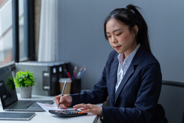 Portrait of a happy young Asian businesswoman celebrating success with arms raised in front of a laptop in the office, freelancer has finished a project.