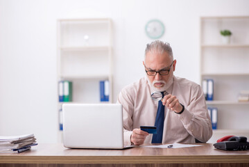 Old male employee holding credit card at workplace
