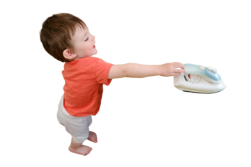 The child's unsafe play with a hot iron in the living room is putting the baby at risk of harm or injury without adult supervision, isolated on white background. Kid aged about two years