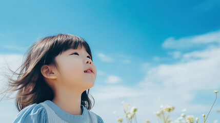 Little Asian girl looking up at the blue sky standing in the  meadow, wind blowing her hair, 5 years old Korean girl, closeup photo portrait, blue sky on background