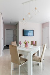 A modern living room combined with a kitchen, in light colors. Dining table with pink tableware