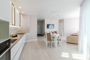 A modern living room combined with a kitchen, in light colors. Dining table with pink tableware