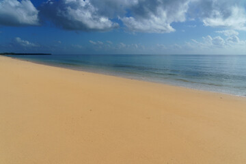 Fototapeta na wymiar sunny blue skies calm ocean water with clouds and a flat sand coastline beach.