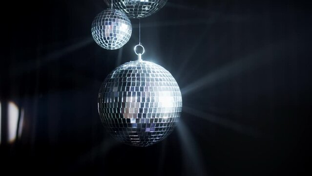 A colorful disco mirror ball illuminates the backdrop of a nightclub. The party lights up the disco ball.