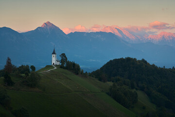 Sunset over The Church of St. Primoz and Felicijan in the village of Jamnik. The last ray of sun on the Alps in Slovenia. Vertical view. - obrazy, fototapety, plakaty