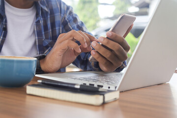 Close up of freelance male hand working on laptop while using a mobile phone. Business and mockup concept