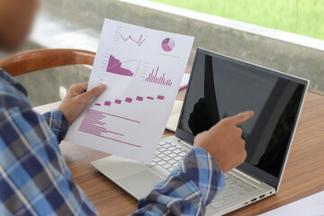 Fototapeta na wymiar Close up of male freelance worker hand working on laptop and pointing with finger on analysis data with business graph and chart of information diagram on office desk in the morning
