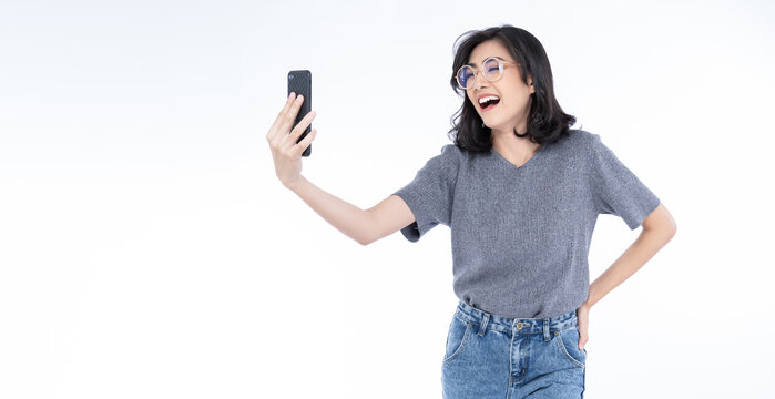 Panoramic banner image of Beautiful Asian woman wearing eyeglasses holding smart mobile phone laughing and smiling while using web app on cellphone isolated on white background. Mockup, web page