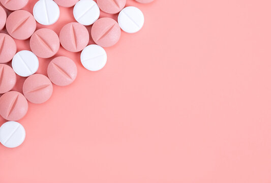 Pink background with pink and white pills in left upper corner. Medical treatment with medicine, vitamins or nutrition supplements in tablets. Hormonal pills in woman health. Copy space for text