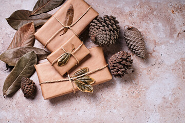Christmas gift packages wrapped in craft paper and pine cones around with dry leaves