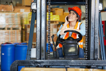 female worker talking by smartphone and driving on forklift in warehouse storage © offsuperphoto