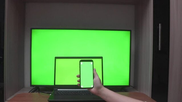 Laptop, HDTV and female hand flipping through mobile phone with green screens, with copy space. Chroma key screen concept for product presentation, online orders and mockup