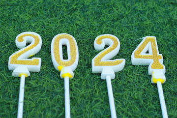 top view of glittering gold candle number 2024 above meadow with green grass, new year eve background concept