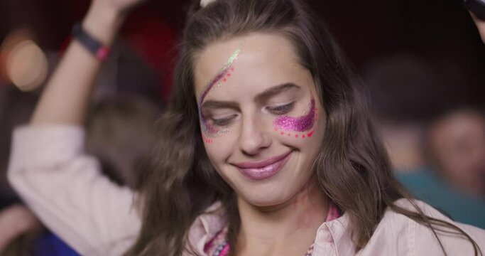 Close up video portrait of a girl with makeup and glitters on her face dancing in front of stage.