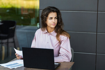 Business woman having a break while sitting in a cafe checking documents, thinking over financial data report or sales chart