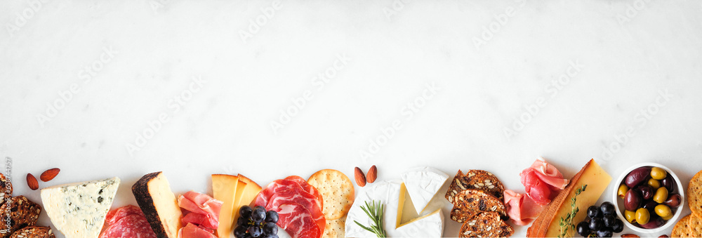 Aufkleber assortment of charcuterie cheeses, meats and appetizers. top view bottom border on a white marble ba