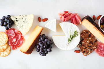 Charcuterie table scene with an assortment of cheeses, meats and appetizers. Above view on a white...