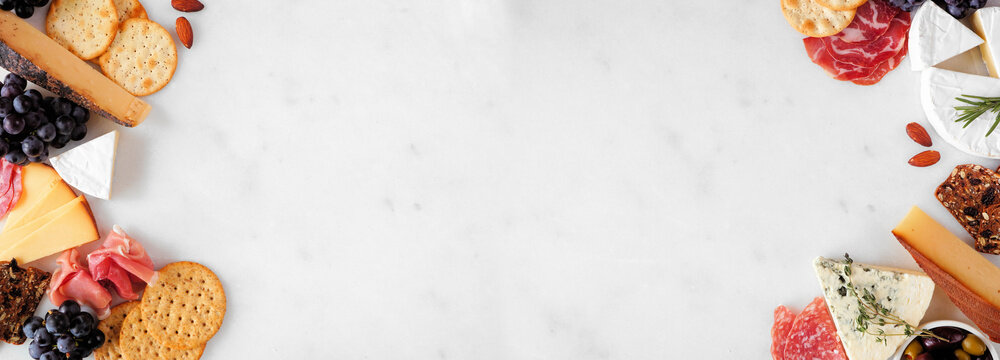 Collection of charcuterie cheeses, meats and appetizers. Top down view double border on a white marble background with copy space.