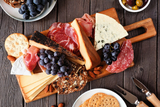 Charcuterie board of a variety of cheeses, meats and appetizers. Above view table scene on a dark wood background.