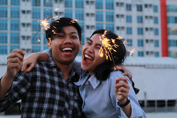 excited asian young couple holding burning sparkler and laughing look at camera to celebrating new...