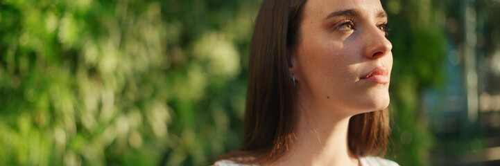 Portrait of young woman with freckles and dark loose hair wearing white top and jeans looks at the...