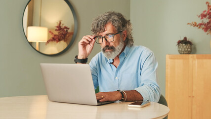 Senior man with gray hair wearing glasses, in living-room using laptop computer