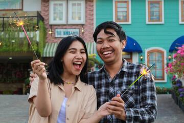 exited asian young couple holding sparkler in the colorful house yard green garden wear stylish...
