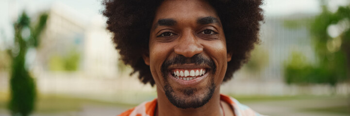 Close-up frontal portrait of young African American man wearing shirt looking at the camera and smiling. Camera moving forwards approaching the person. Lifestyle concept.